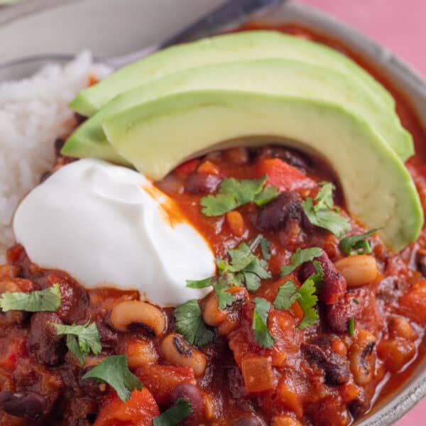 A bowl of three bean chilli with rice, sliced avocado and soured cream.
