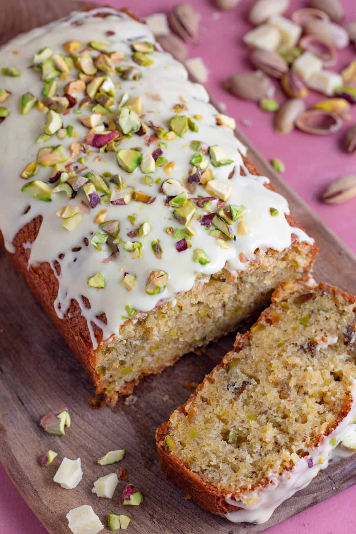 A gluten free pistachio loaf cake with a slice taken off, topped with white chocolate and pistachio nuts.