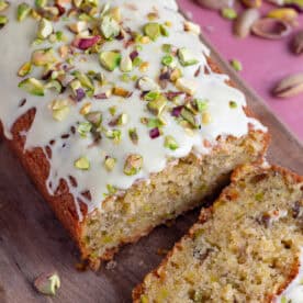 A gluten free pistachio loaf cake with a slice taken off, topped with white chocolate and pistachio nuts.