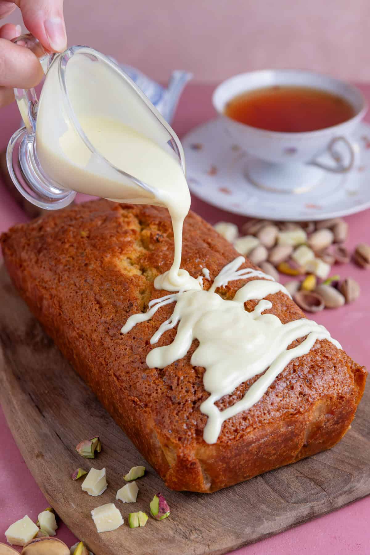Process shot of pistachio cake recipe showing white chocolate being poured onto the cake.