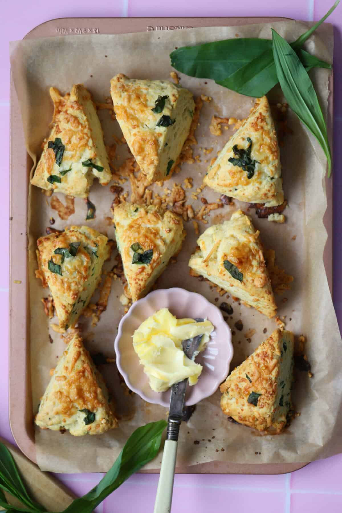A pink baking tray filled with cheese and wild garlic scones and a small butter dish.