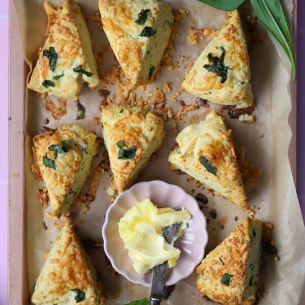 A pink baking tray filled with cheese and wild garlic scones and a small butter dish.