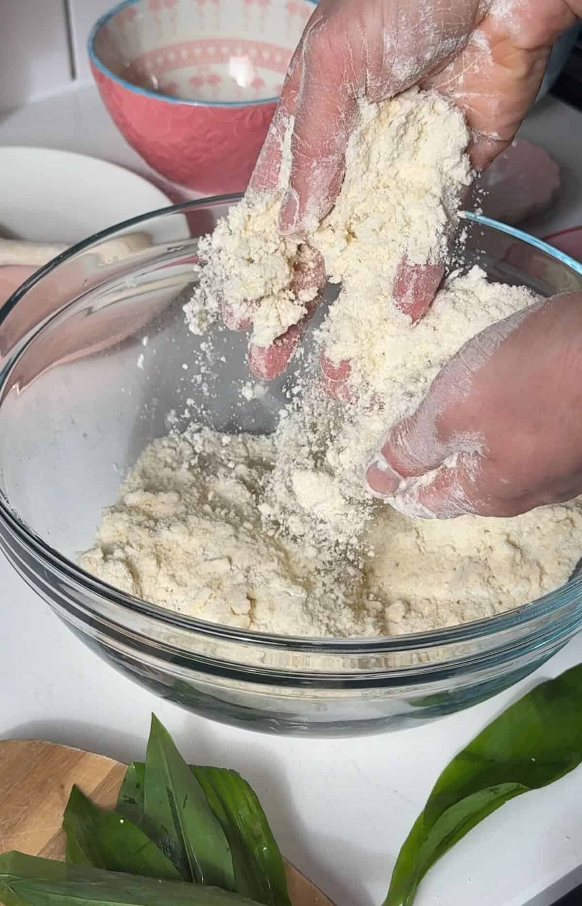 Process shot of cheese and wild garlic scones recipe showing hands rubbing the butter into the gluten free flour mix.