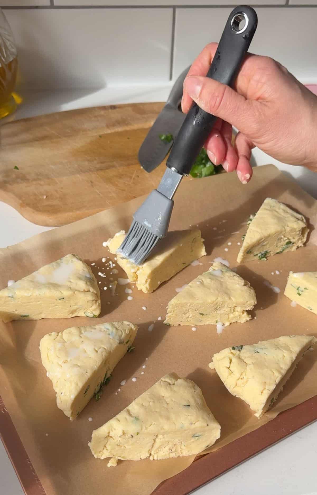 Process shot of cheese and wild garlic scones recipe showing the wedges being brushed with milk.