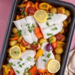 Overhead shot of a cod and chorizo traybake in a roasting tin with lemon slices on top.