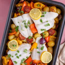 Overhead shot of a cod and chorizo traybake in a roasting tin with lemon slices on top.