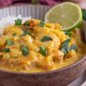 A bowl of fish curry in a creamy coconut sauce, with a slice of lime on the side.