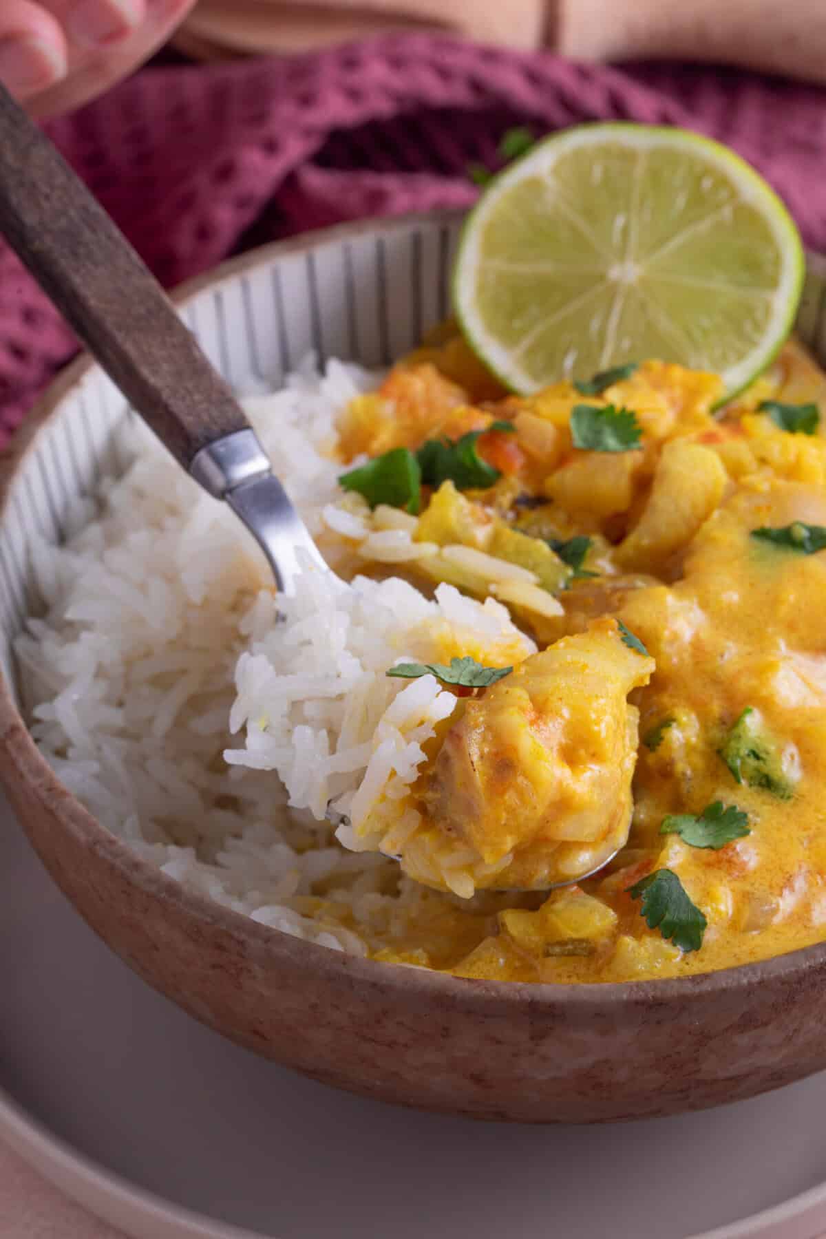 A bowl of fish curry in a creamy coconut sauce, with a slice of lime on the side.