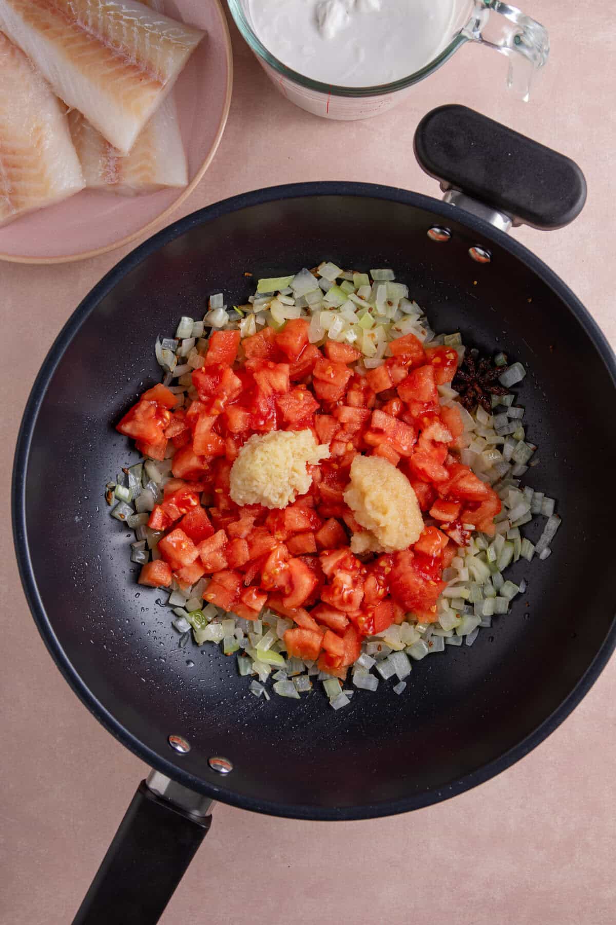 Adding tomatoes, garlic and ginger to the onions in a pan.