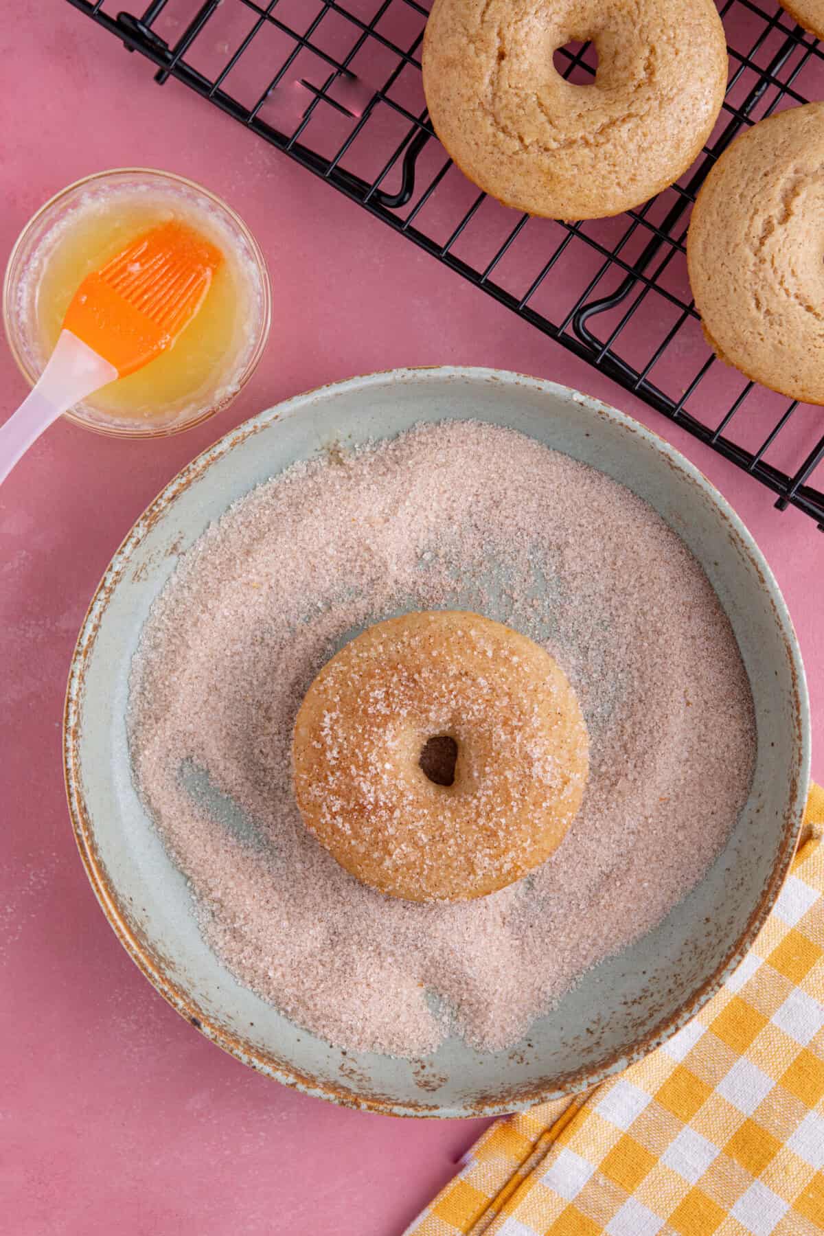 Process shot for gluten free doughnuts recipe showing the donuts being coated in sugar.