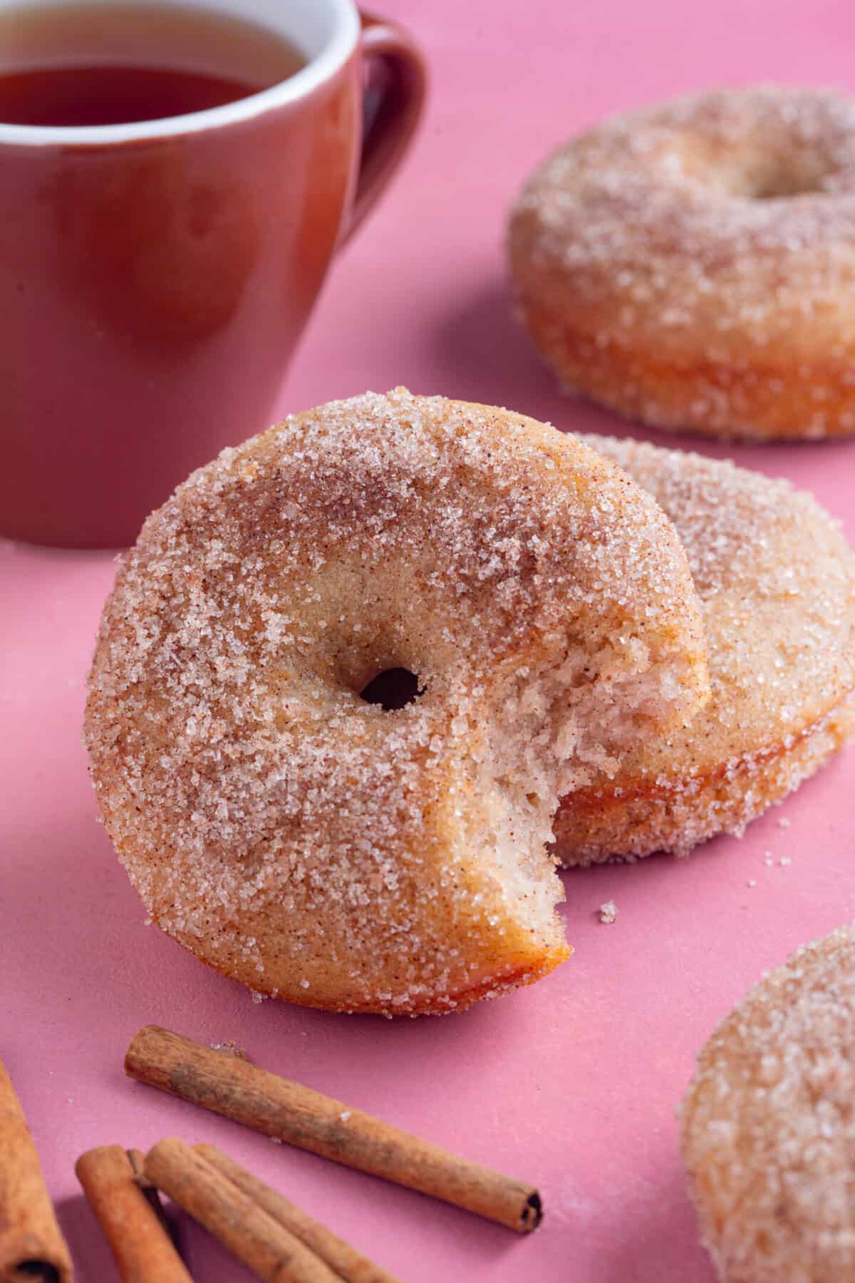 A gluten free doughnut with a bite taken out of it and a cup of tea in the backgound.
