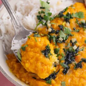 A bowl of red lentil dahl with rice and a spoon.