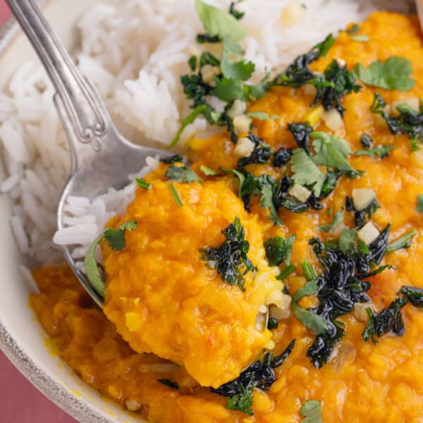 A bowl of red lentil dahl with rice and a spoon.