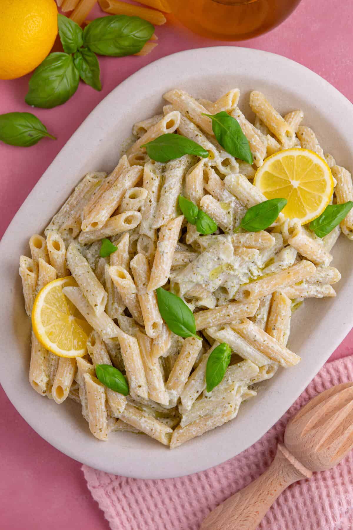 A serving dish of creamy ricotta and pesto pasta with basil and a lemon slice.