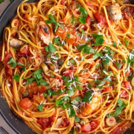 A pan with spaghetti, sardines, olives and capers in a rich tomato sauce, garnished with parsley.
