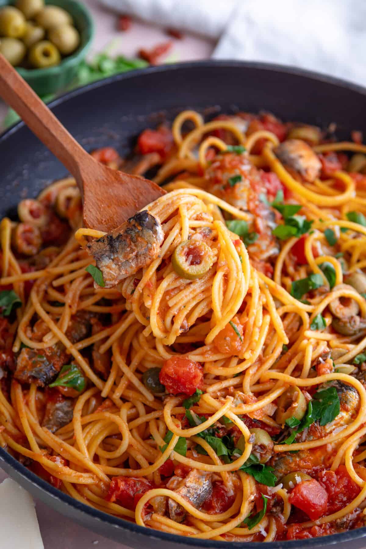 A wooden spoon portioning out some sardine spaghetti.