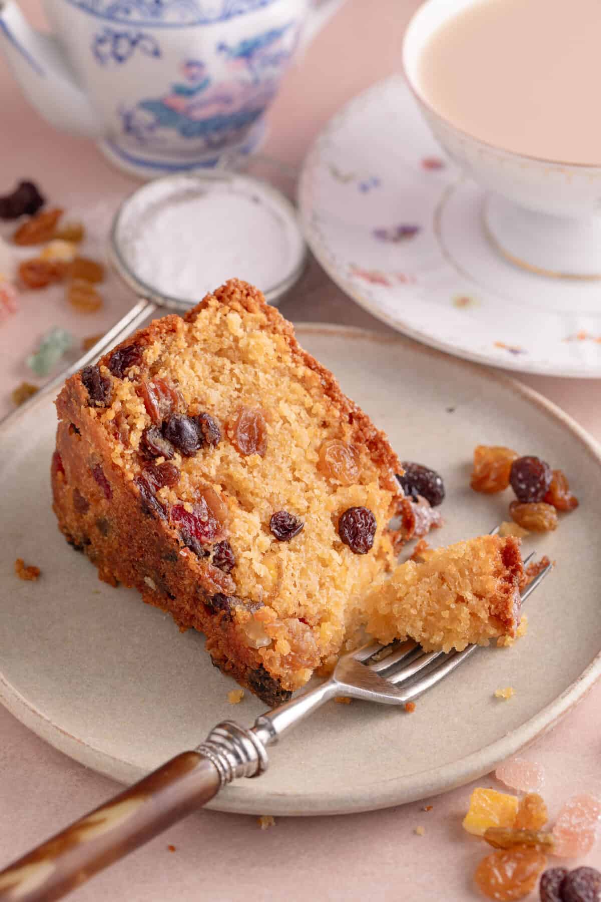 A slice of gluten free fruit cake on a plate with a forkful removed.