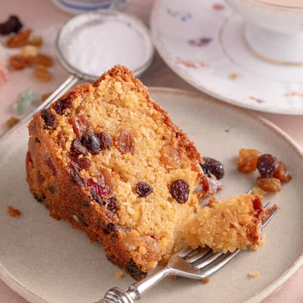 A slice of gluten free fruit cake on a plate with a forkful removed.