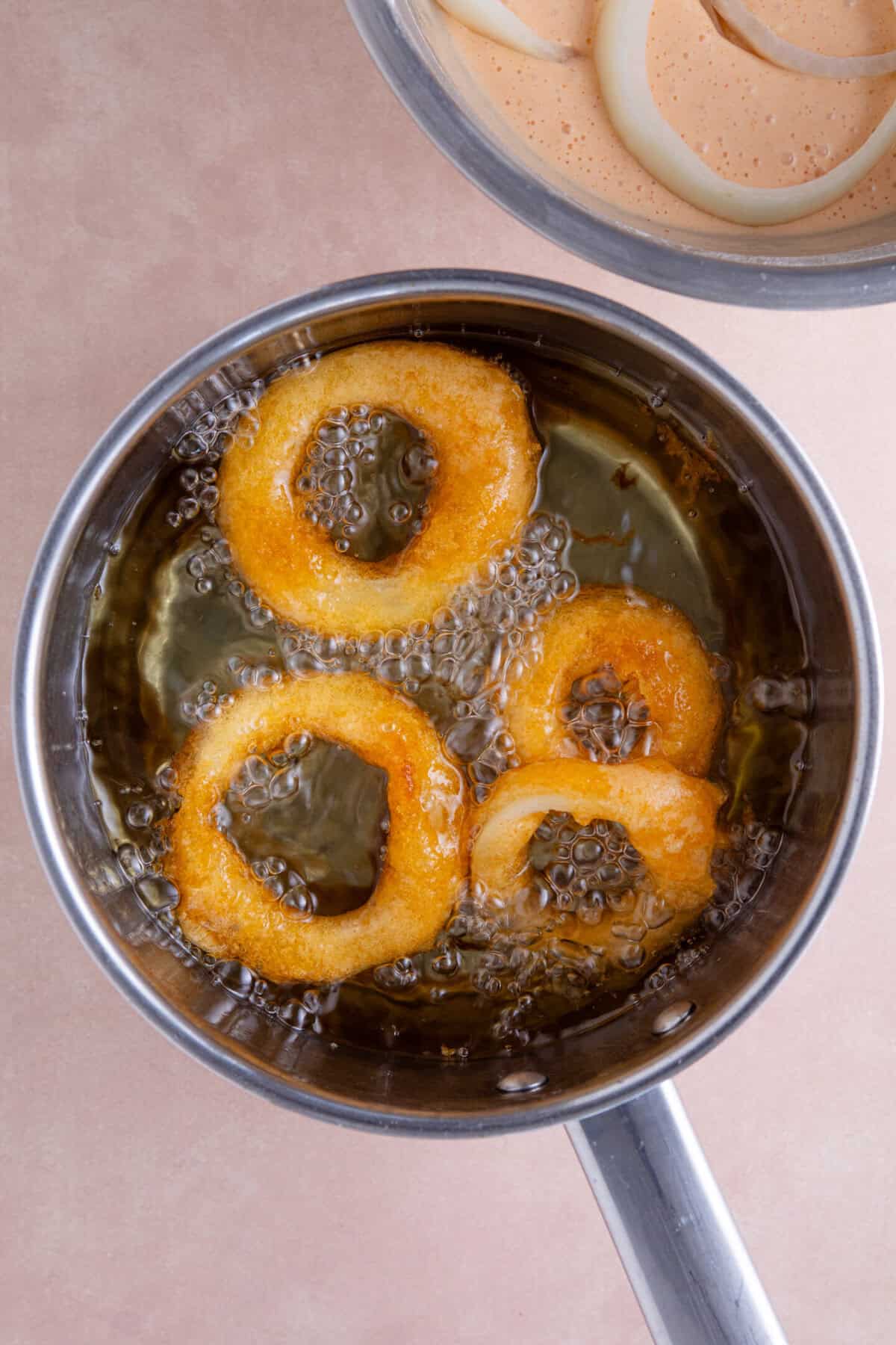 Onion rings frying in a pan of hot oil.