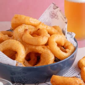 A bowl of gluten free onion rings with a pint of gluten free lager in the background.