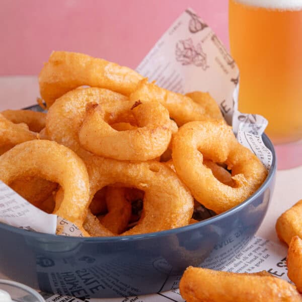 A bowl of gluten free onion rings with a pint of gluten free lager in the background.