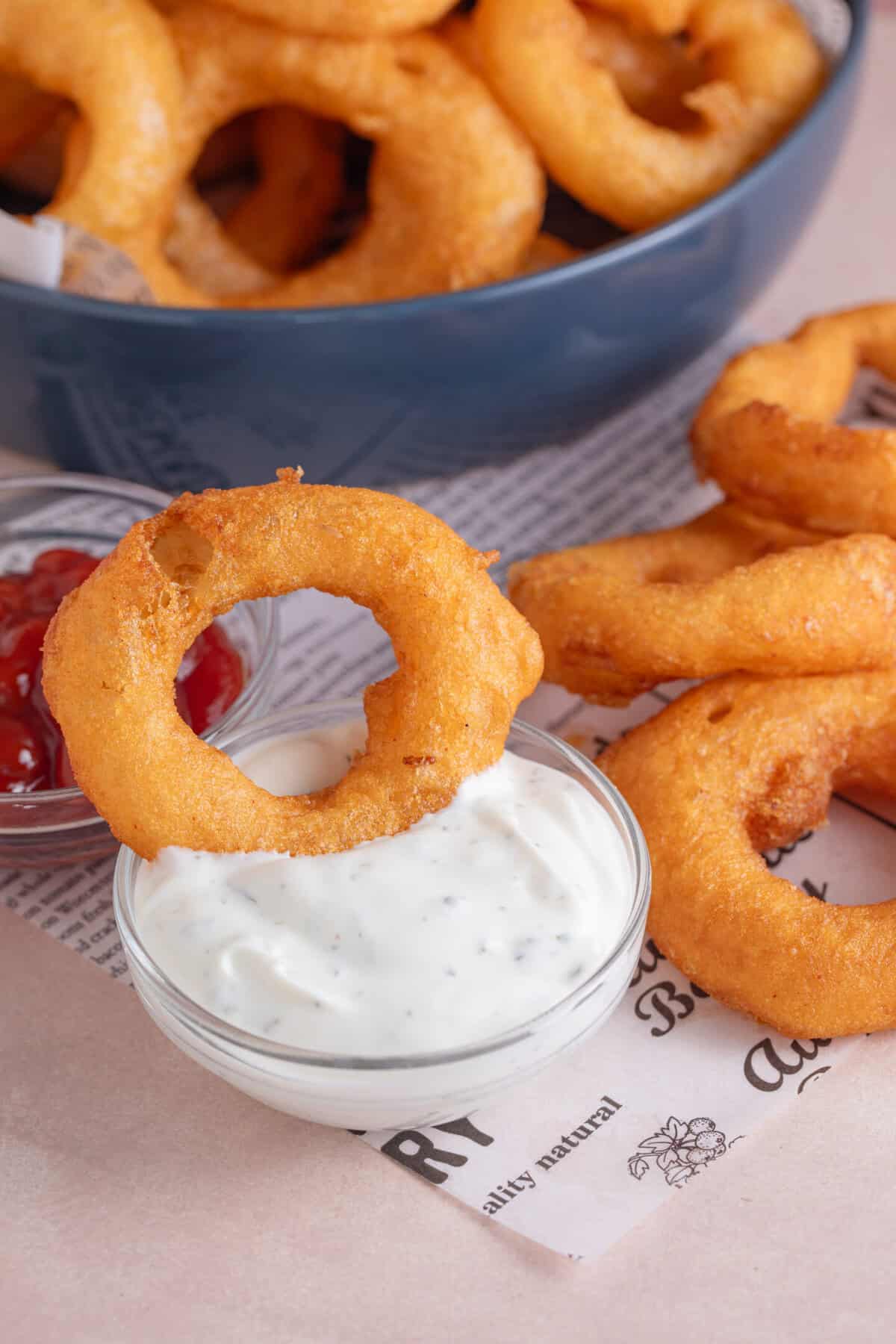 A gluten free onion ring being dipped into some garlic mayo.