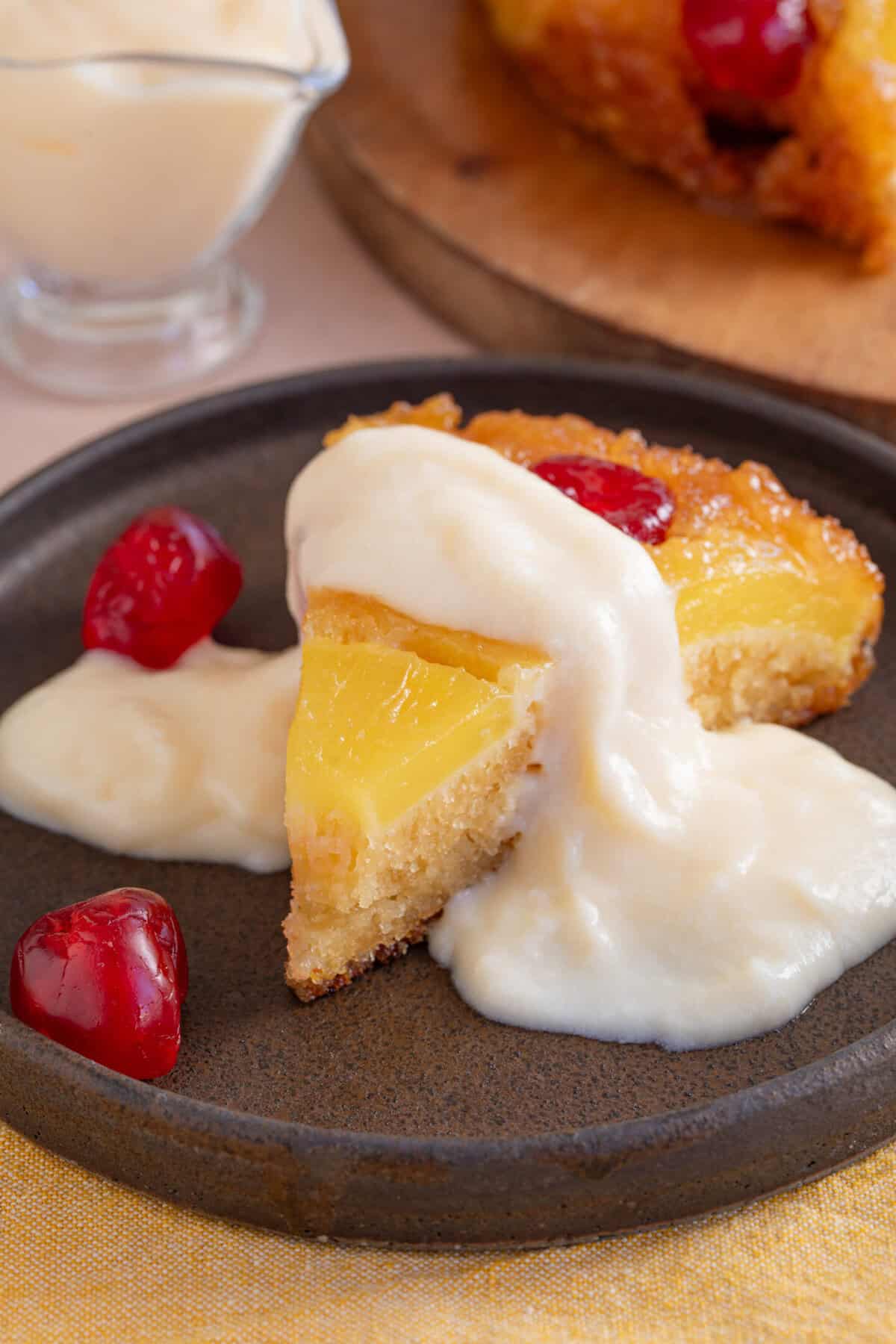 A slice of gluten free pineapple upside down cake on a plate with custard on top.