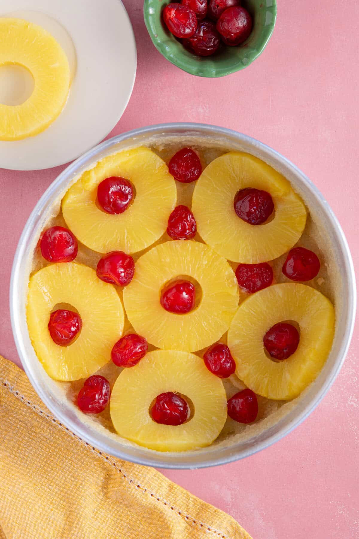 Process shot of a pineapple upside down cake showing the pineapple and cherries arranged in the tin.