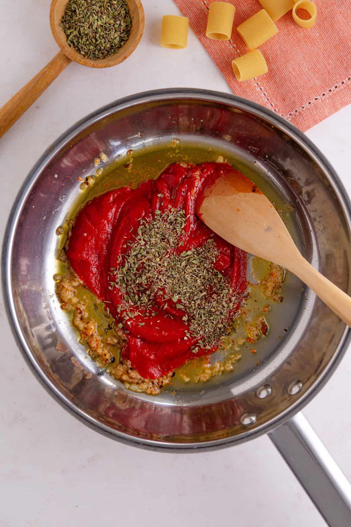 Process shot of tomato burrata pasta recipe showing the tomato paste and Italian herbs added to the pan.