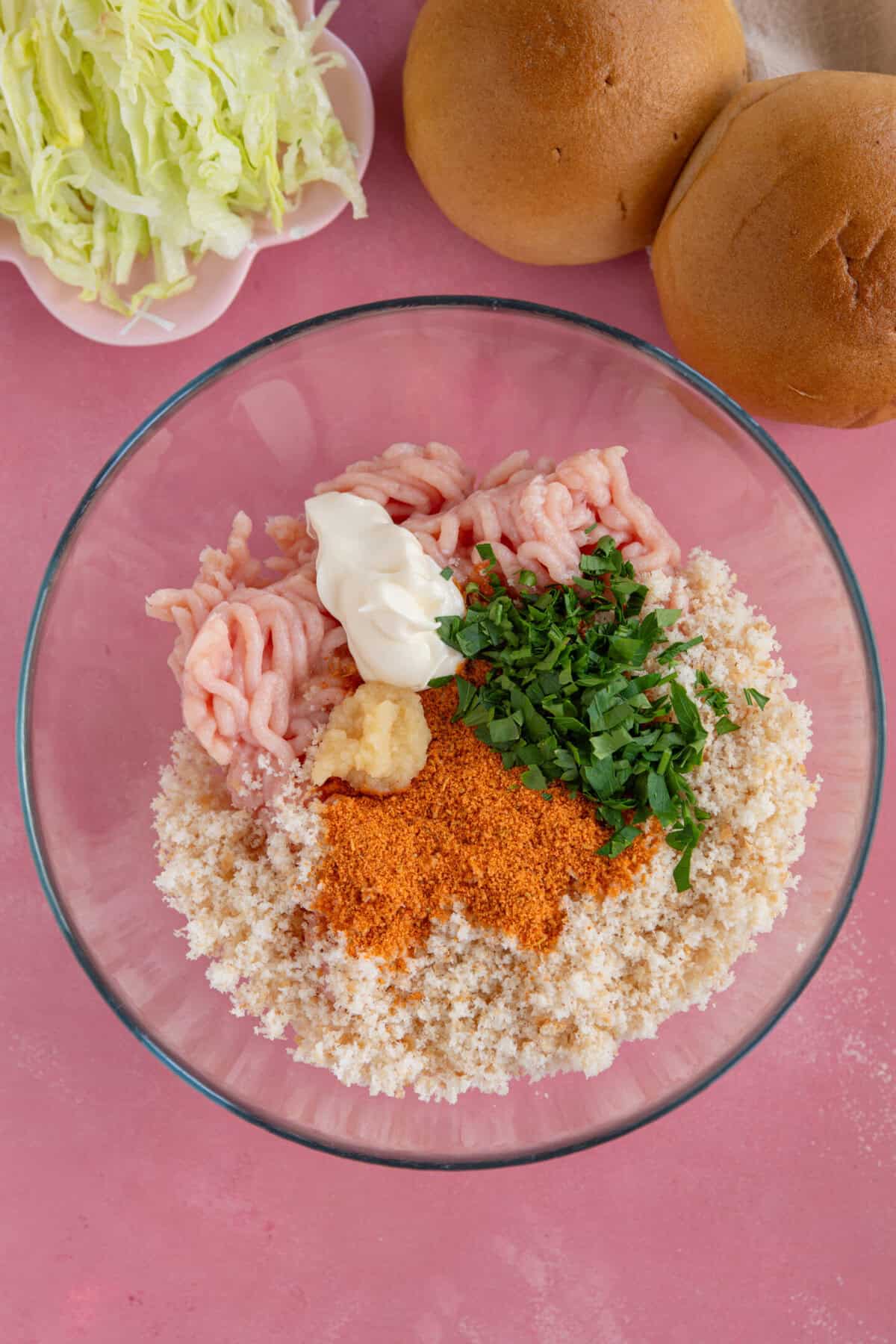 Process shot for chicken mince burgers showing the ingredients added to a glass mixing bowl.