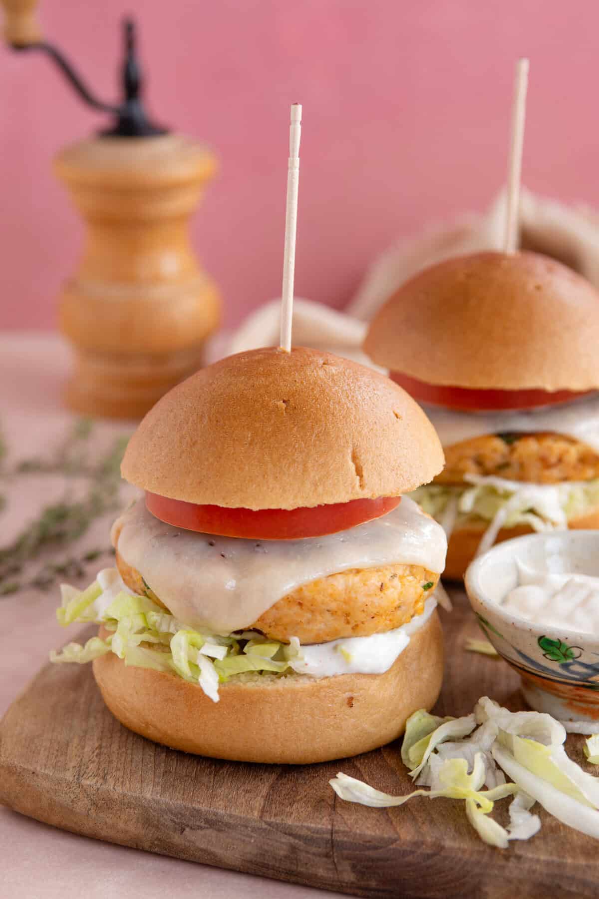 Gluten free chicken burgers on a board with cheese a tomato slice.