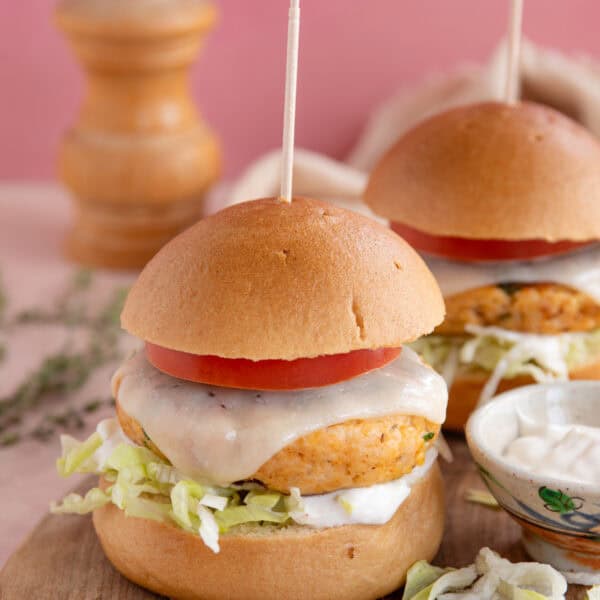 Gluten free chicken burgers on a board with cheese a tomato slice.