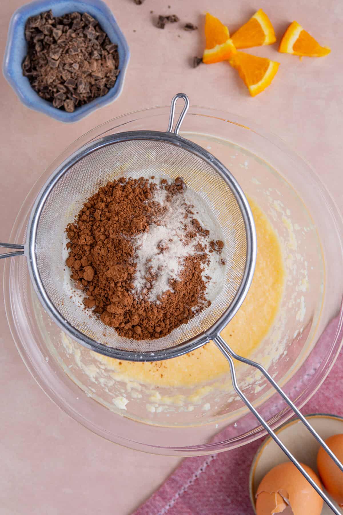 Process shot of gluten free chocolate orange cupcakes showing the cocoa and flour being sifted into the bowl.