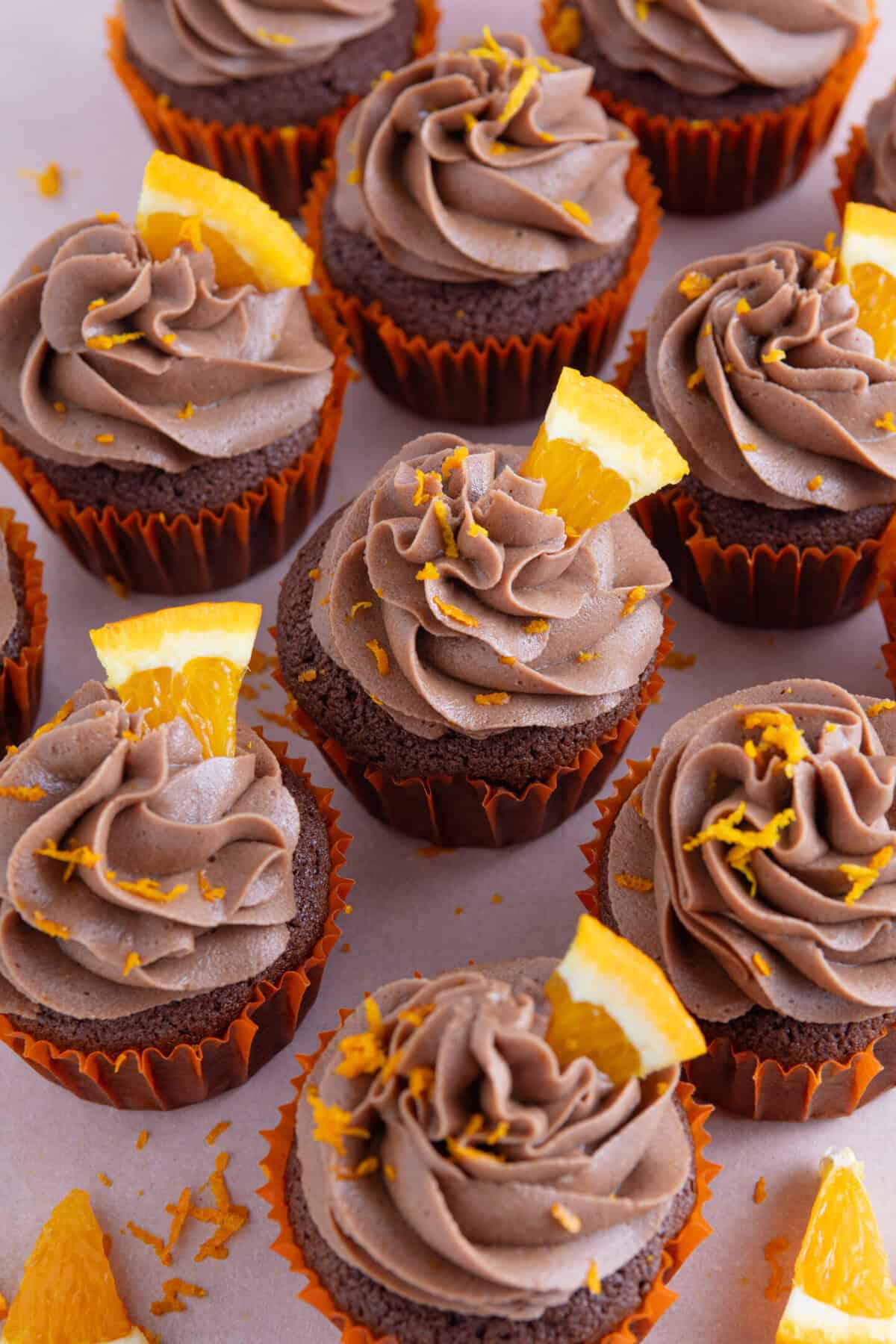 A collection of gluten free chocolate orange cupcakes with wedges of orange on top.