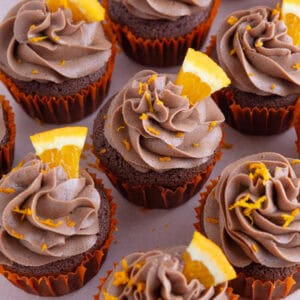 A collection of gluten free chocolate orange cupcakes with wedges of orange on top.