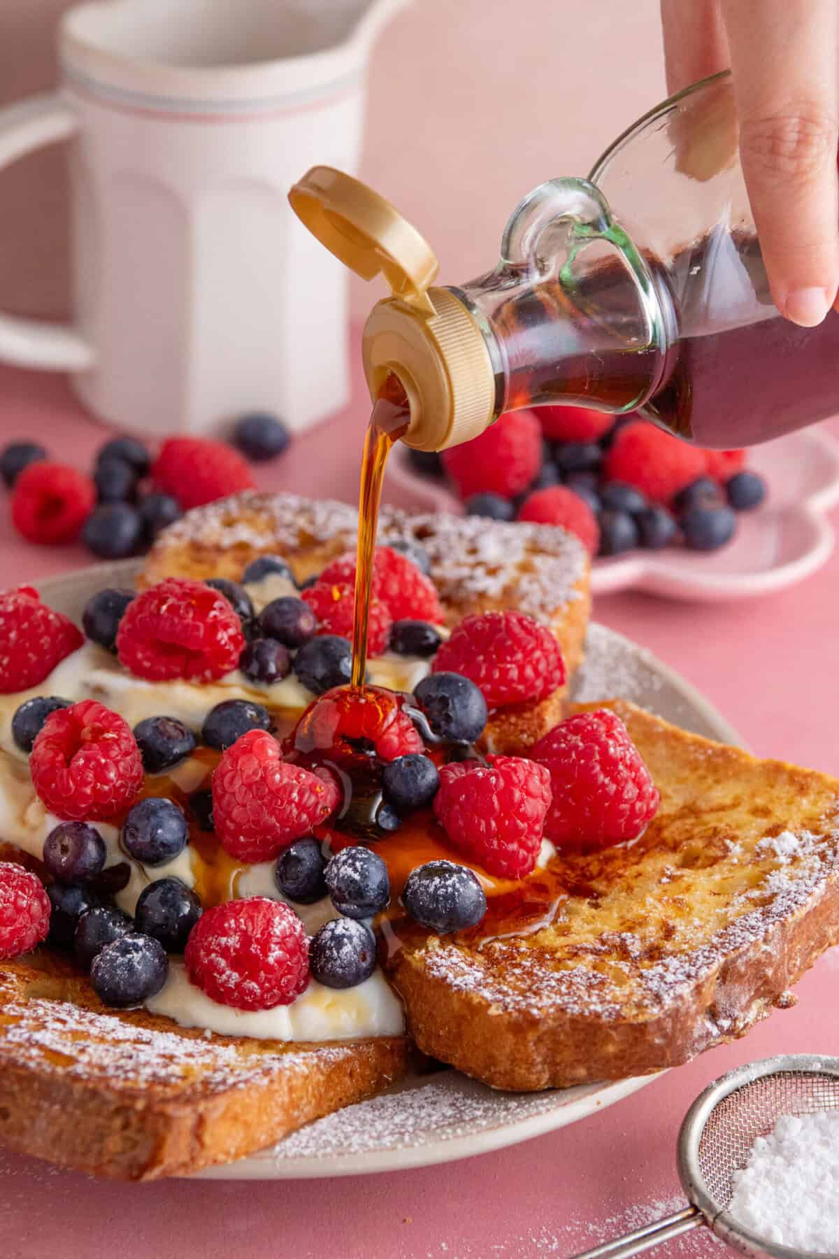 Maple syrup being drizzled over a plate of gluten free French toast, yoghurt and berries.