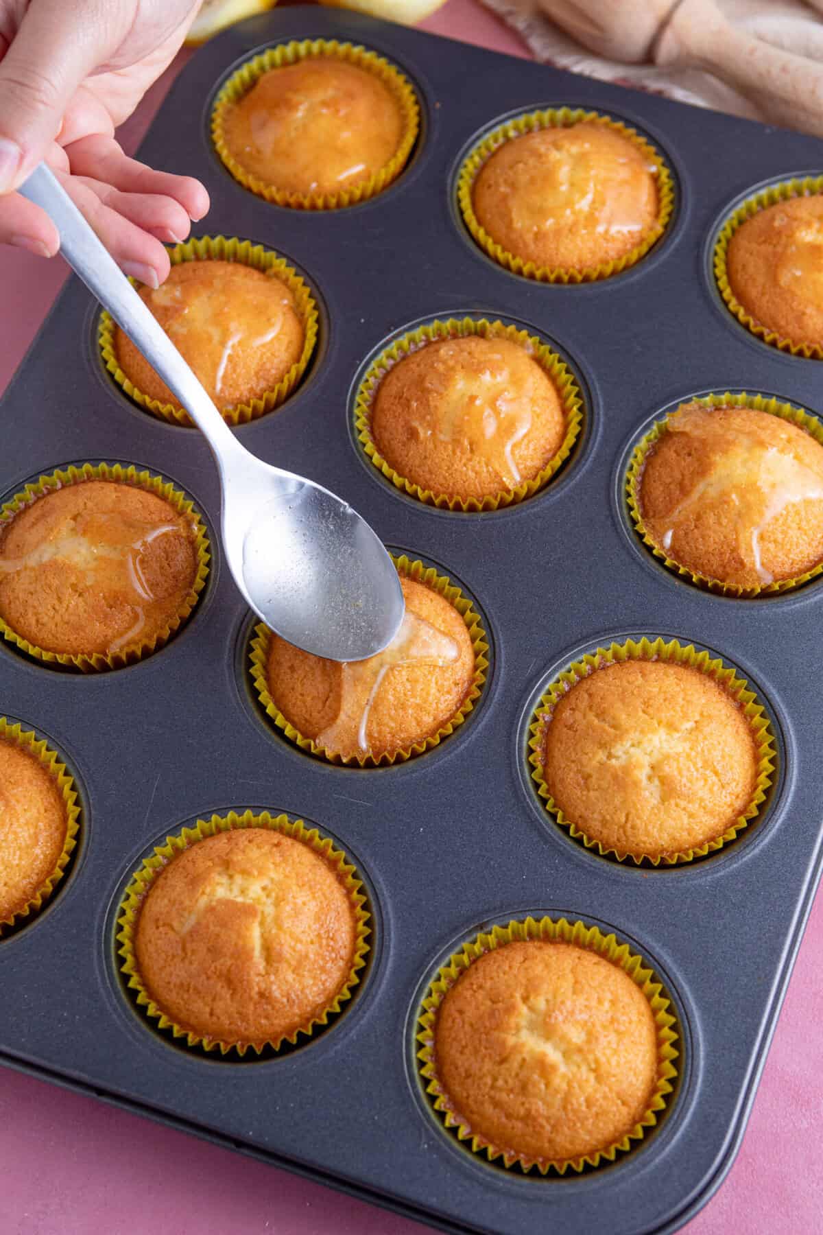 Process shot for gluten free lemon drizzle cupcakes showing the syrup being spooned onto the cupcakes.