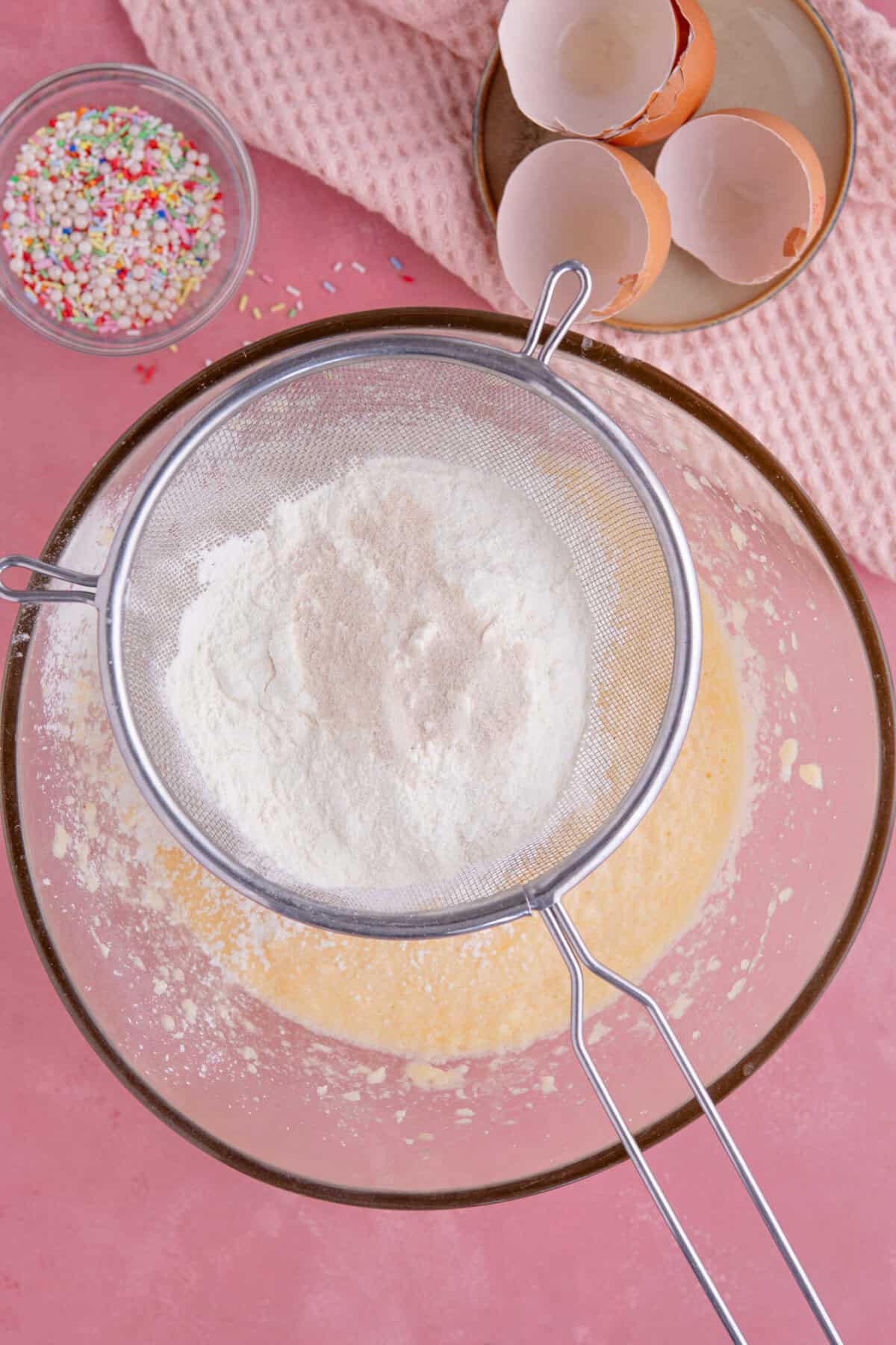 Process shot of gluten free vanilla cupcakes showing the flour being sieved into the mixing bowl.