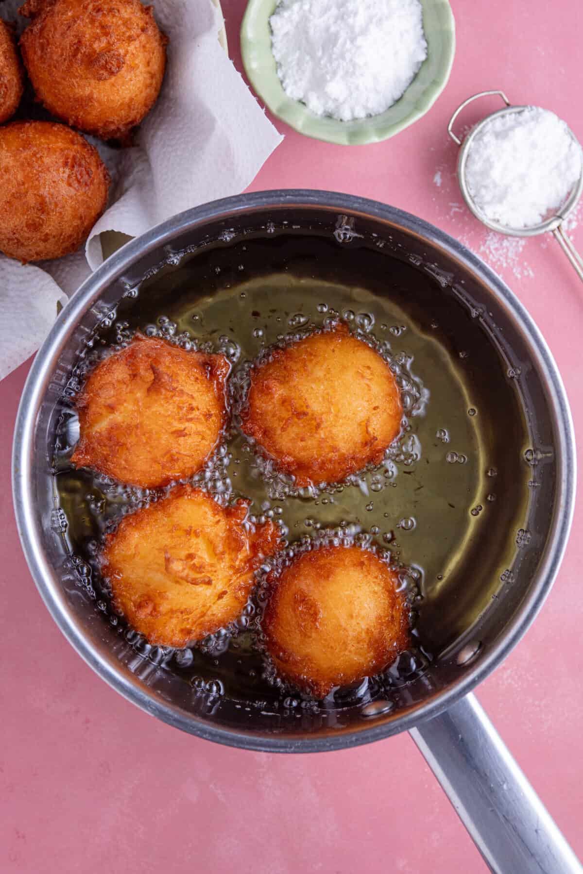 Process shot for gluten free zeppole showing the dough deep frying in a pan of oil.