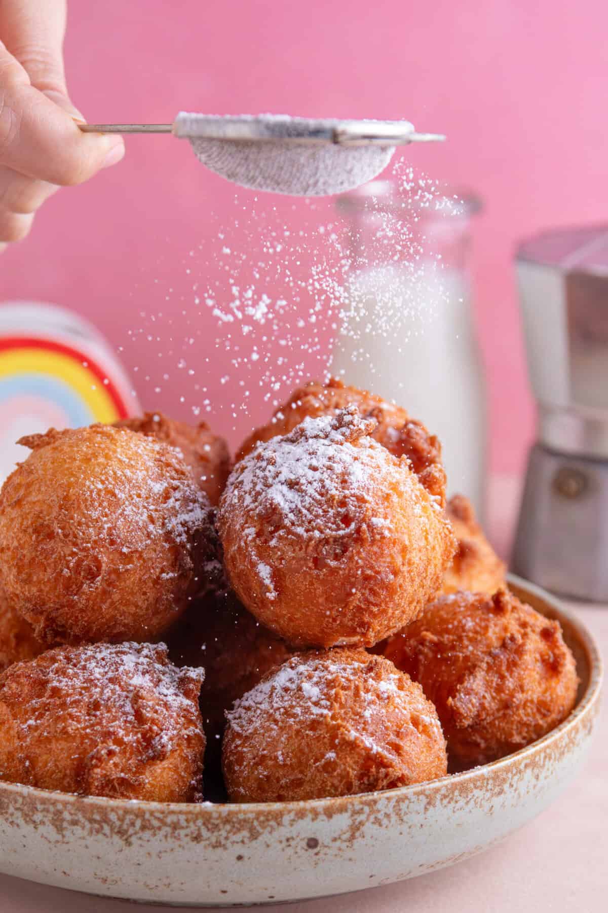 Process shot for gluten free zeppole showing the dough balls being dusted with icing sugar.