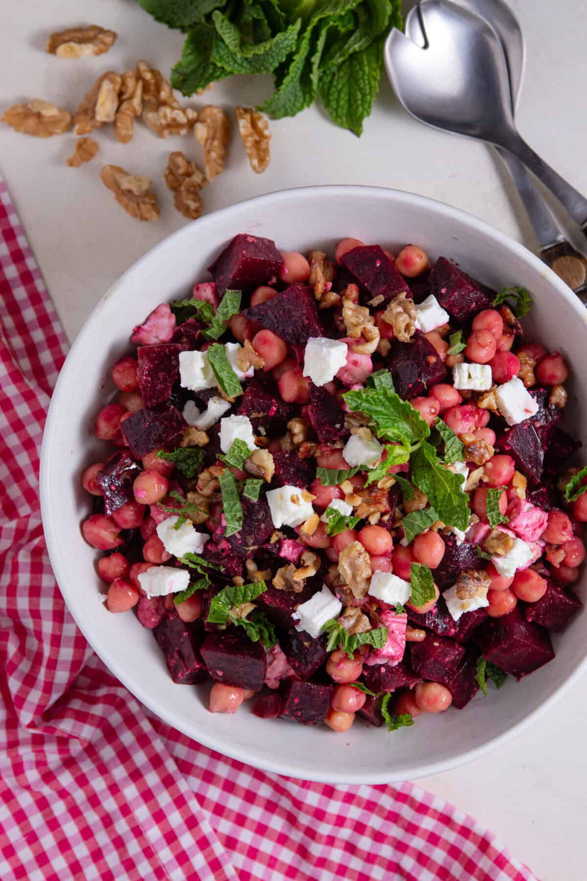A bowl of beetroot, feta and walnut salad with serving spoons.
