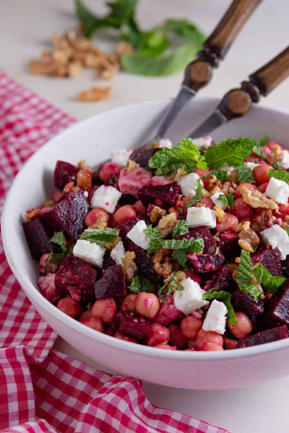 A bowl of beetroot, feta and walnut salad with serving spoons.
