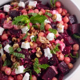 A bowl of beetroot salad with feta, chickpeas, olive and fresh mint on top.