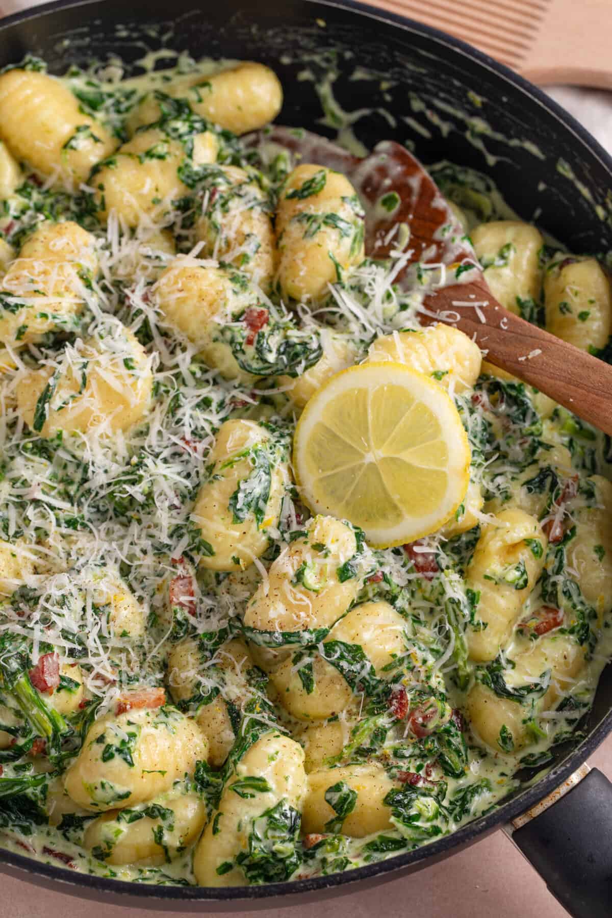 Close up of creamy gnocchi with spinach and bacon in a pan.