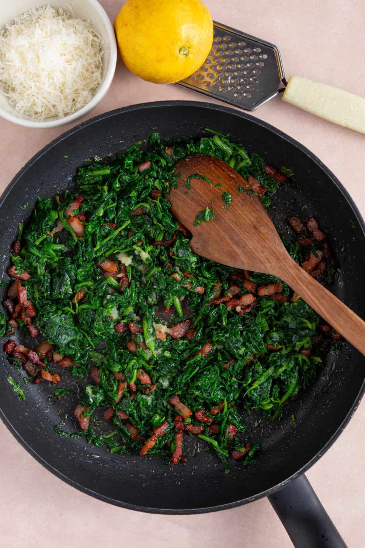 Process shot of creamy gnocchi recipe showing the spinach and bacon in a pan.