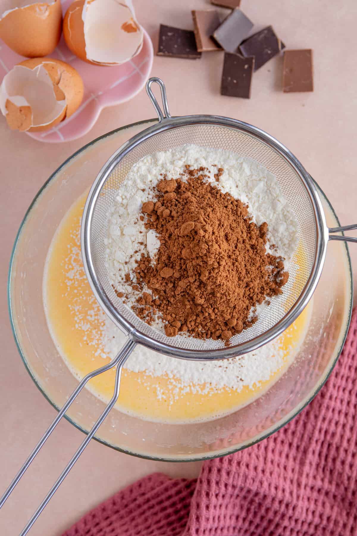 Process shot of a gluten free chocolate loaf cake recipe showing the flour and cocoa powder being sifted into the cake batter.