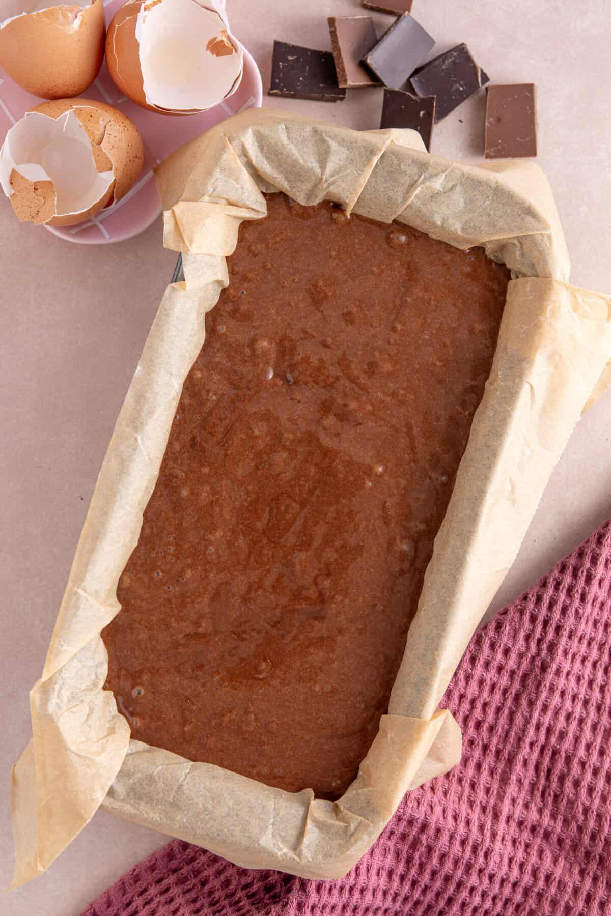 Process shot of a gluten free chocolate loaf cake recipe showing the cake batter in a lined loaf tin.