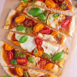 Gluten free flatbread pizza topped with tomato, pesto and basil and cut into strips.