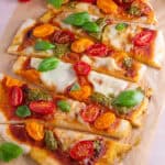 Gluten free flatbread pizza topped with tomato, pesto and basil and cut into strips.