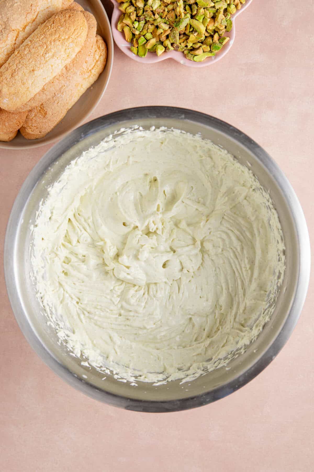 Process shot of a pistachio tiramisu recipe showing the whipped pistachio cream in a large bowl.